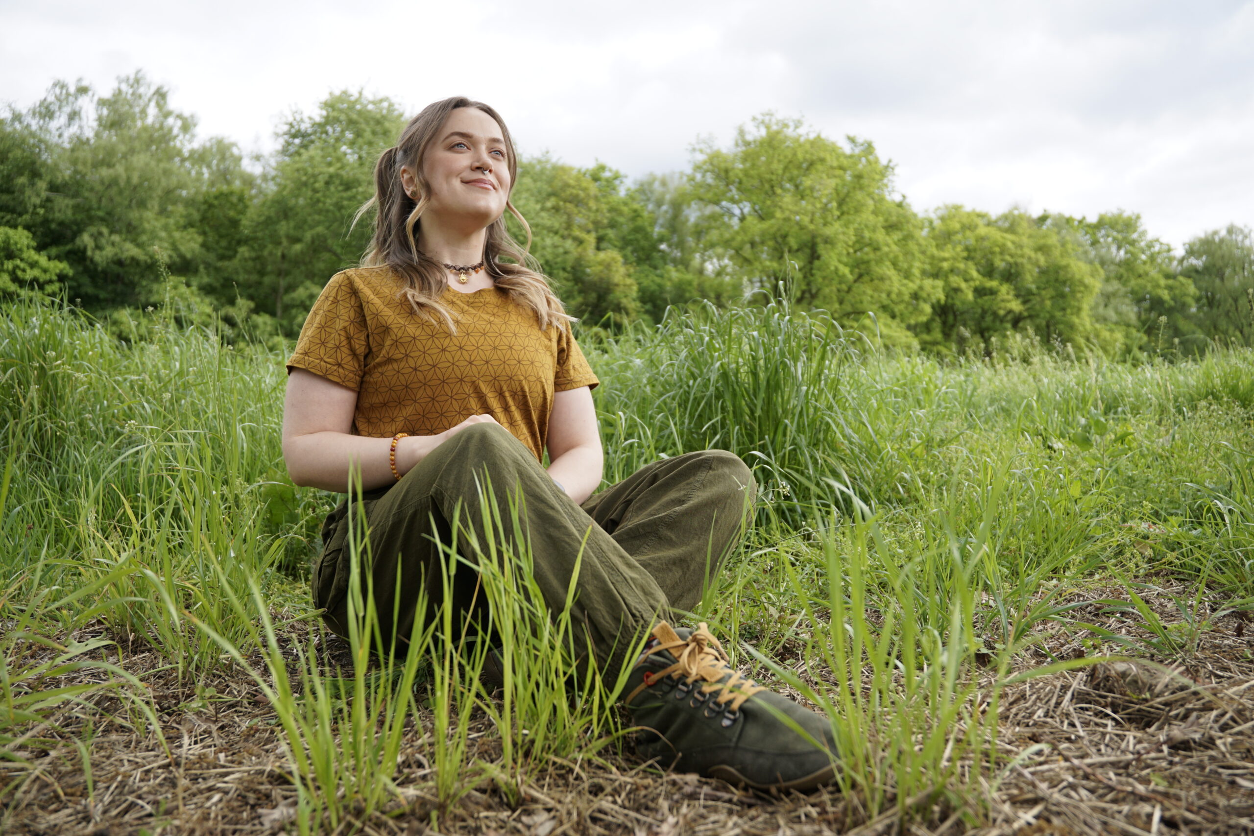 Person sitzt lächelnd in einem Feld mit hohem Gras und genießt die Natur