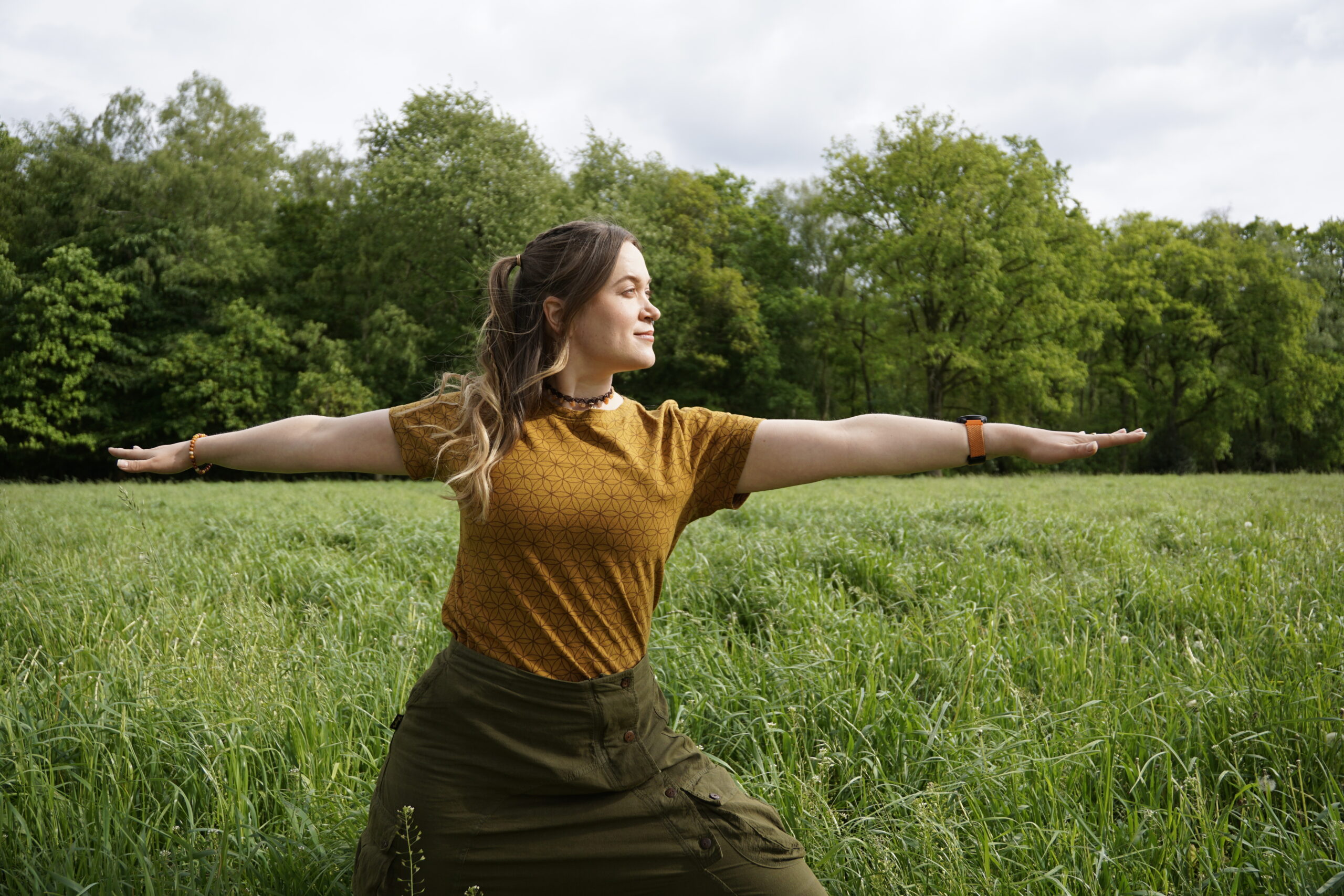 Frau auf grüner, hoher Wiese in der Yogapose Krieger 2